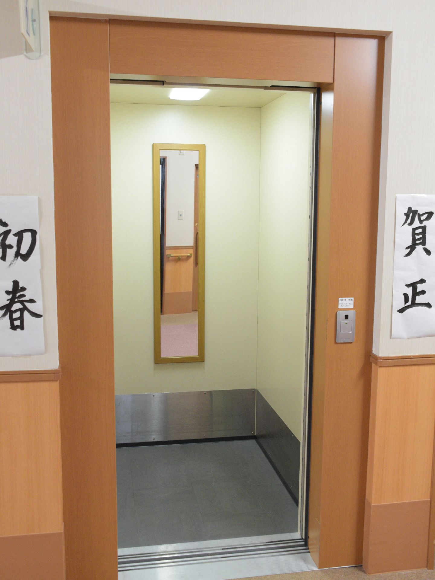 白い壁面には書が飾られている。エレベーター周辺は木目調になっており、内部には細長い鏡も設置されている。