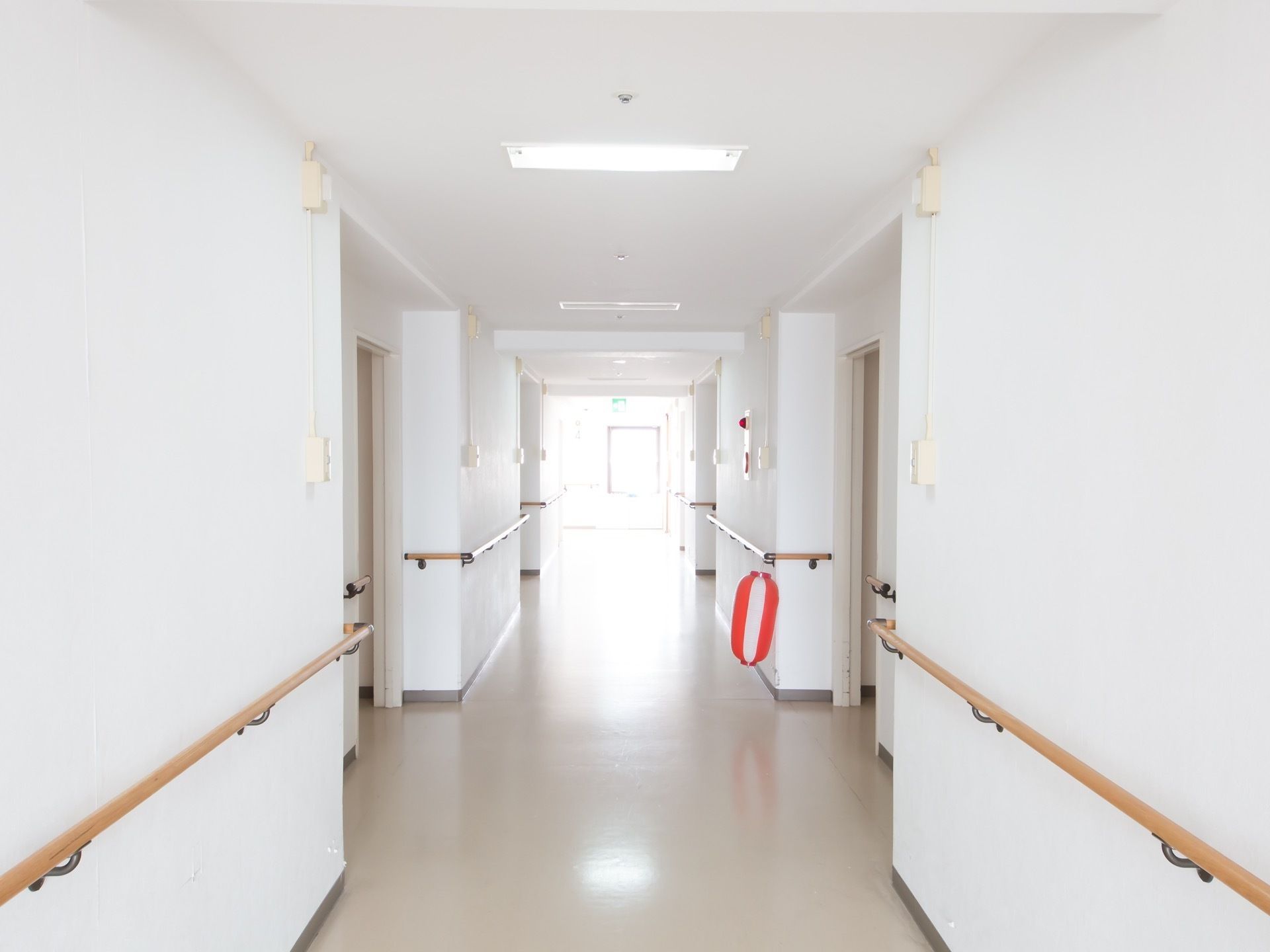 床も壁も白で統一された通路である。突き当りに窓があるので明るい。壁には木製の手すりが設置されている。