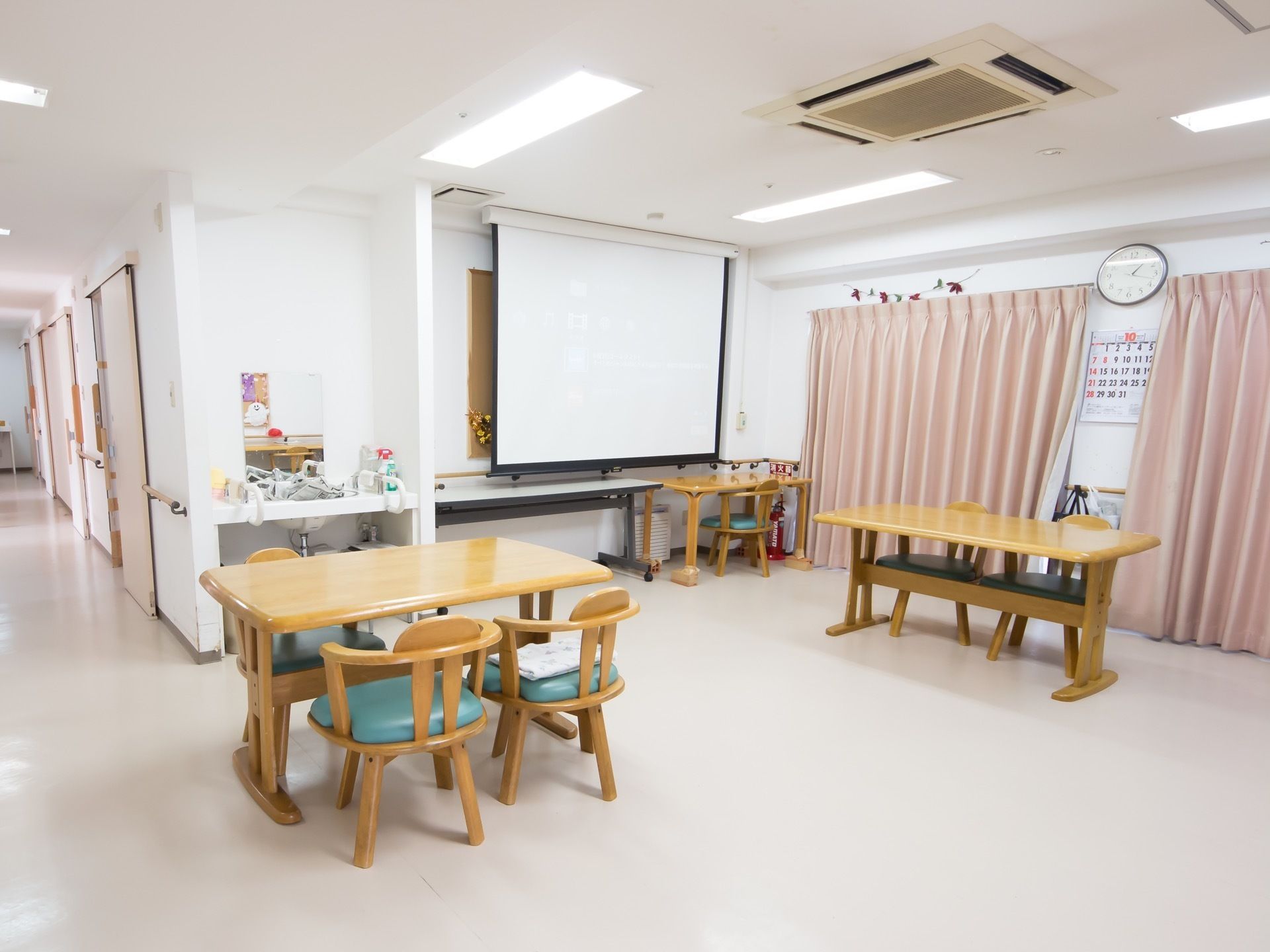 通路の一角に共有スペースがあり、木製のテーブルセットが2つ置かれている。洗面台があり、壁には映像スクリーンが掛かっている。