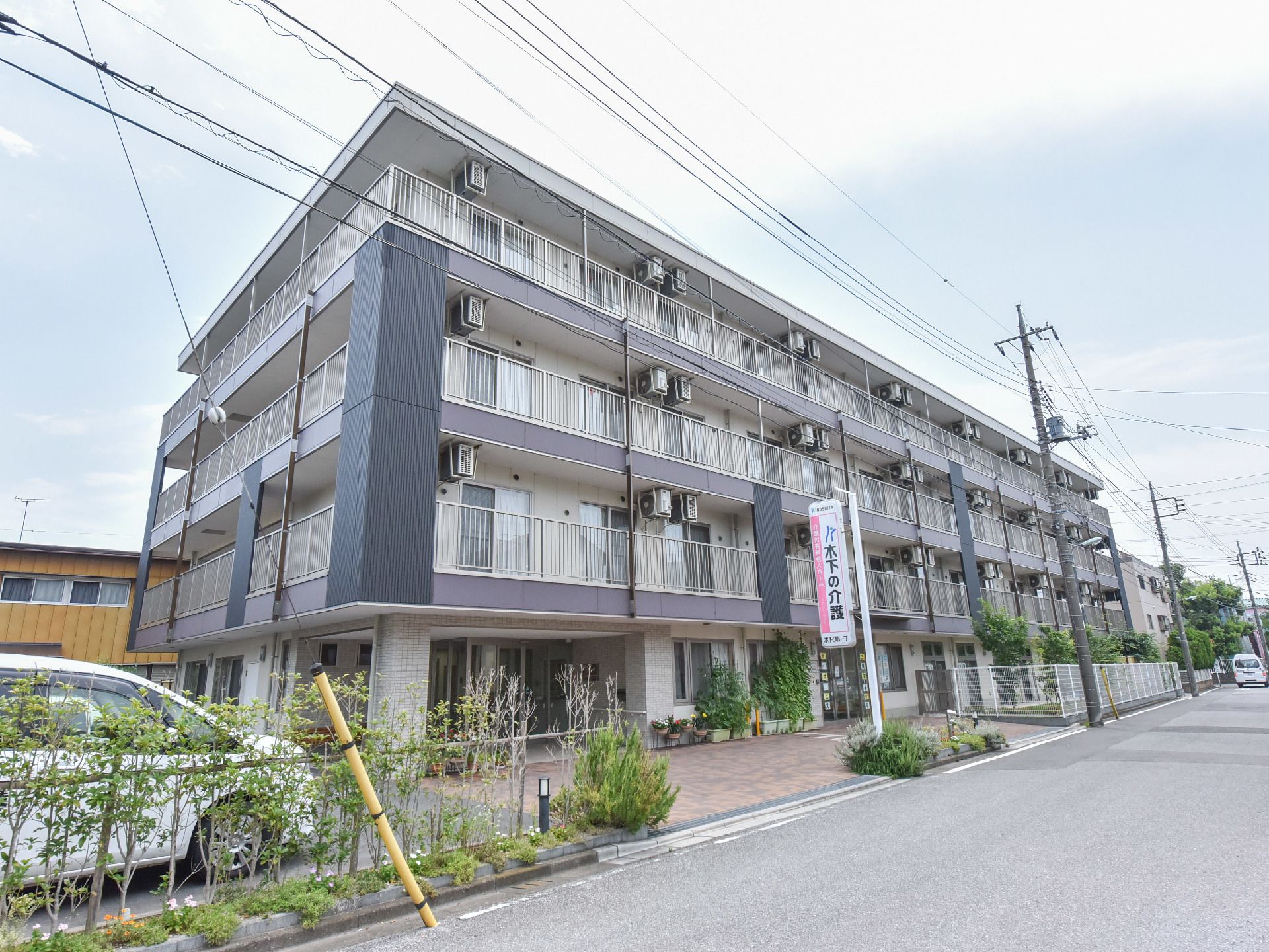 施設の前方には、アスファルト舗装された広い道路がある。周りには高い建物もなく、ライトブルーの空と白い雲が見える。