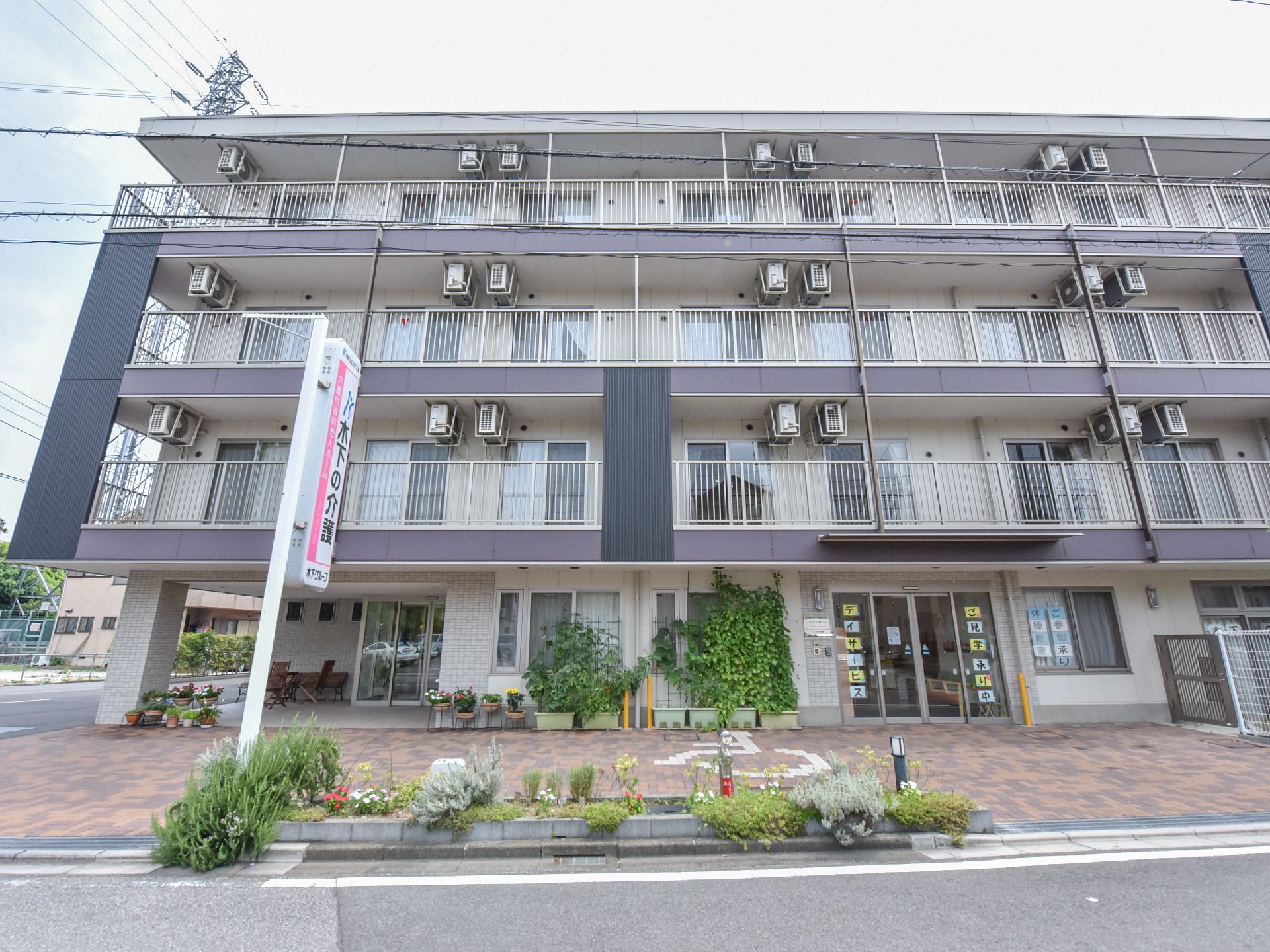 ライトグレーとダークグレーが組み合わされたデザインのシックな外観となっている。壁際には、植木鉢やプランターが並べられている。