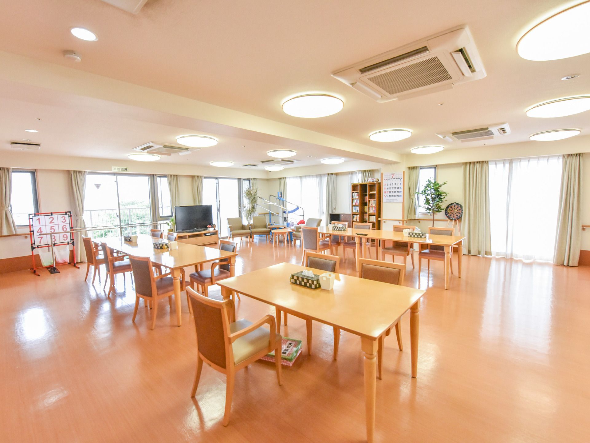 リビングの壁には、たくさんの大きな窓があり、明るい光が差し込んでいる。奥の方には、縦長の大きな本棚が設置されている。