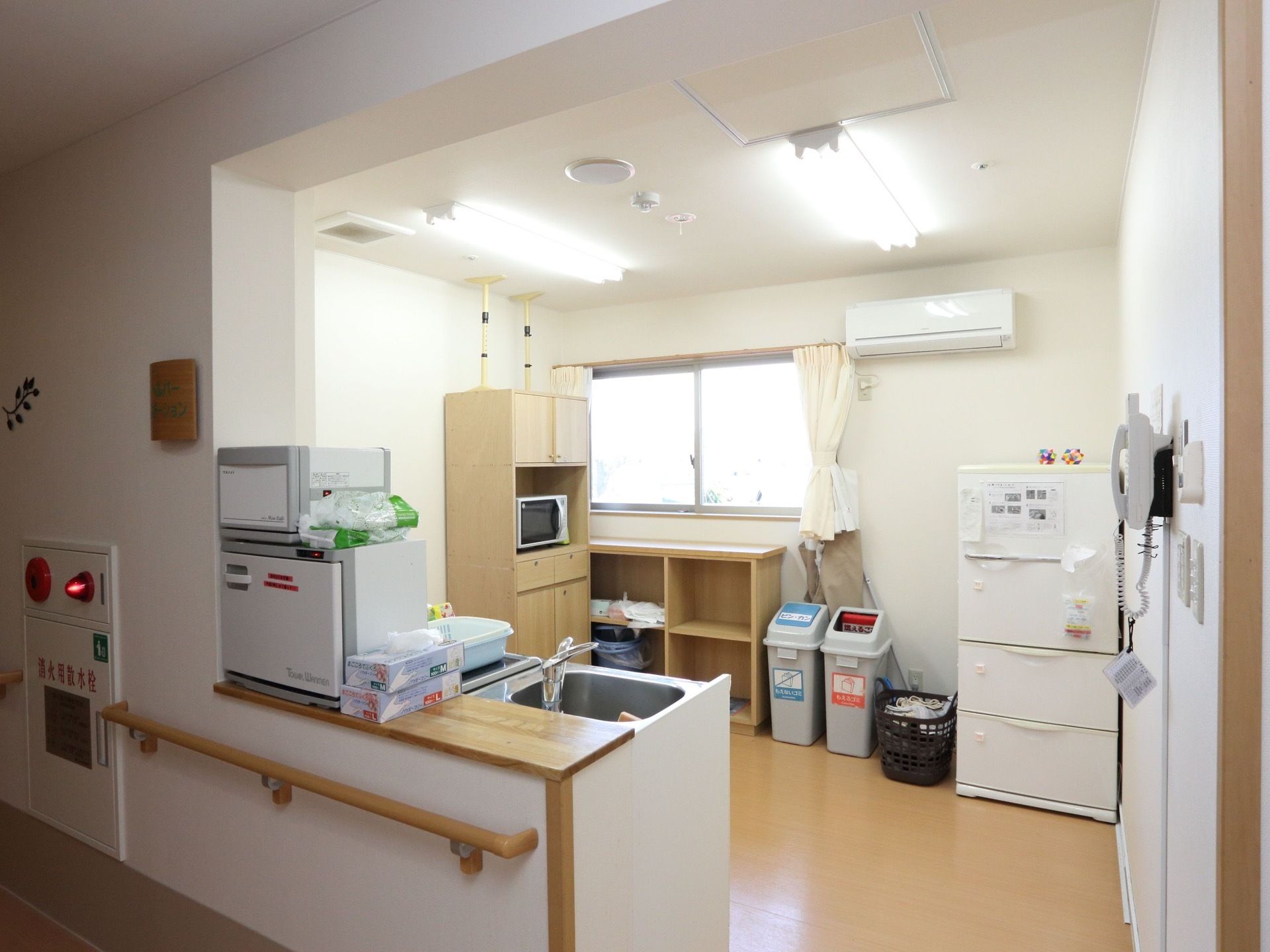 白い冷蔵庫が、キッチンスペースの右端に設置されている。その横に、茶色のカゴとグレーのゴミ箱が２つ置いてある。