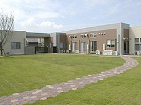 ベージュ色のモダンな2階建て建物の手前には、広い芝生広場とレンガの小道