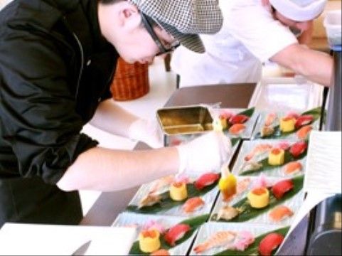 バランの上に寿司を盛る、眼鏡と帽子を身に着けたスタッフ