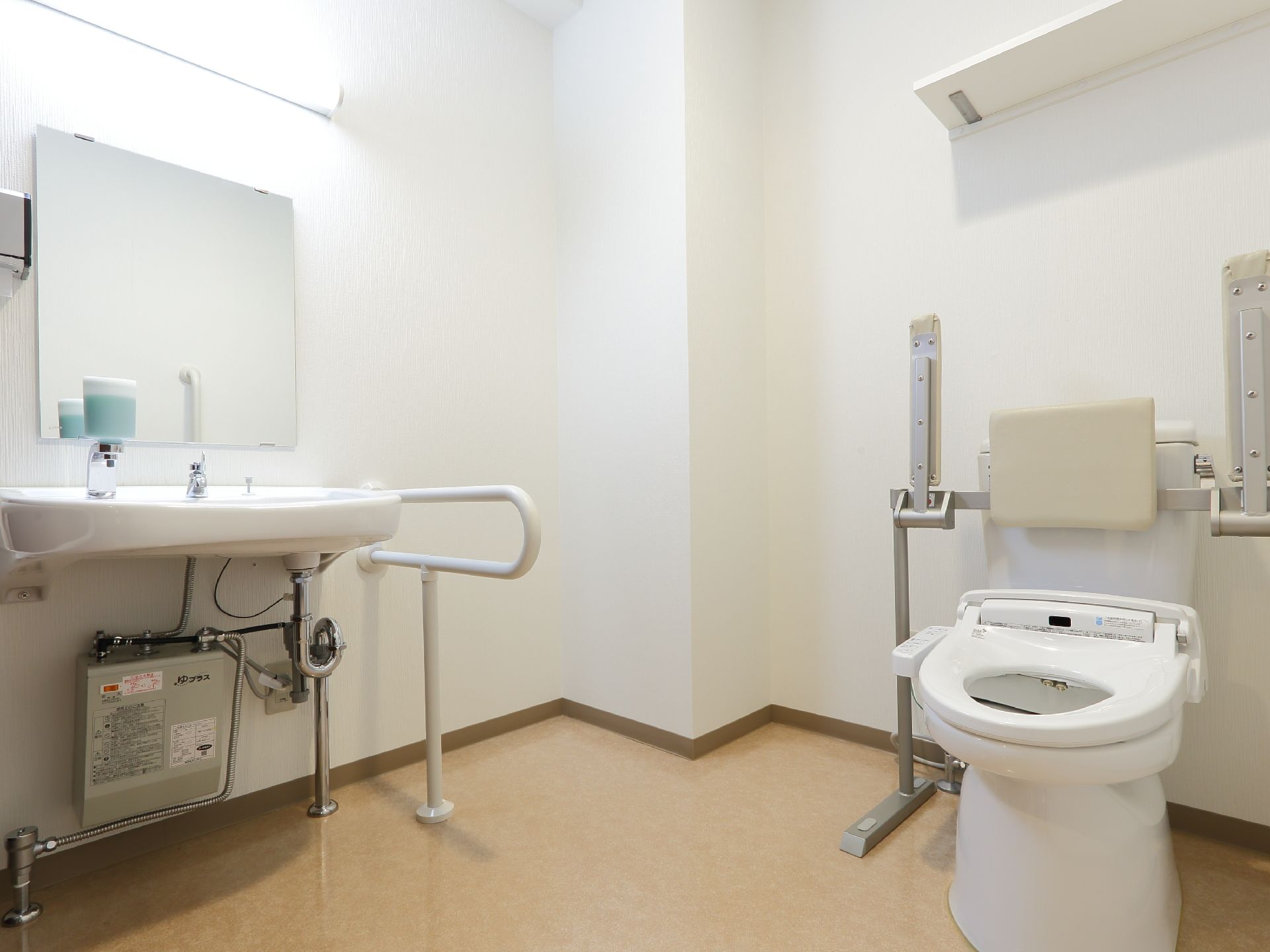 広々とした空間のトイレには洗面台も設置されている。洋式便器には背もたれ付きのひじ掛け手すりが備え付けられている。
