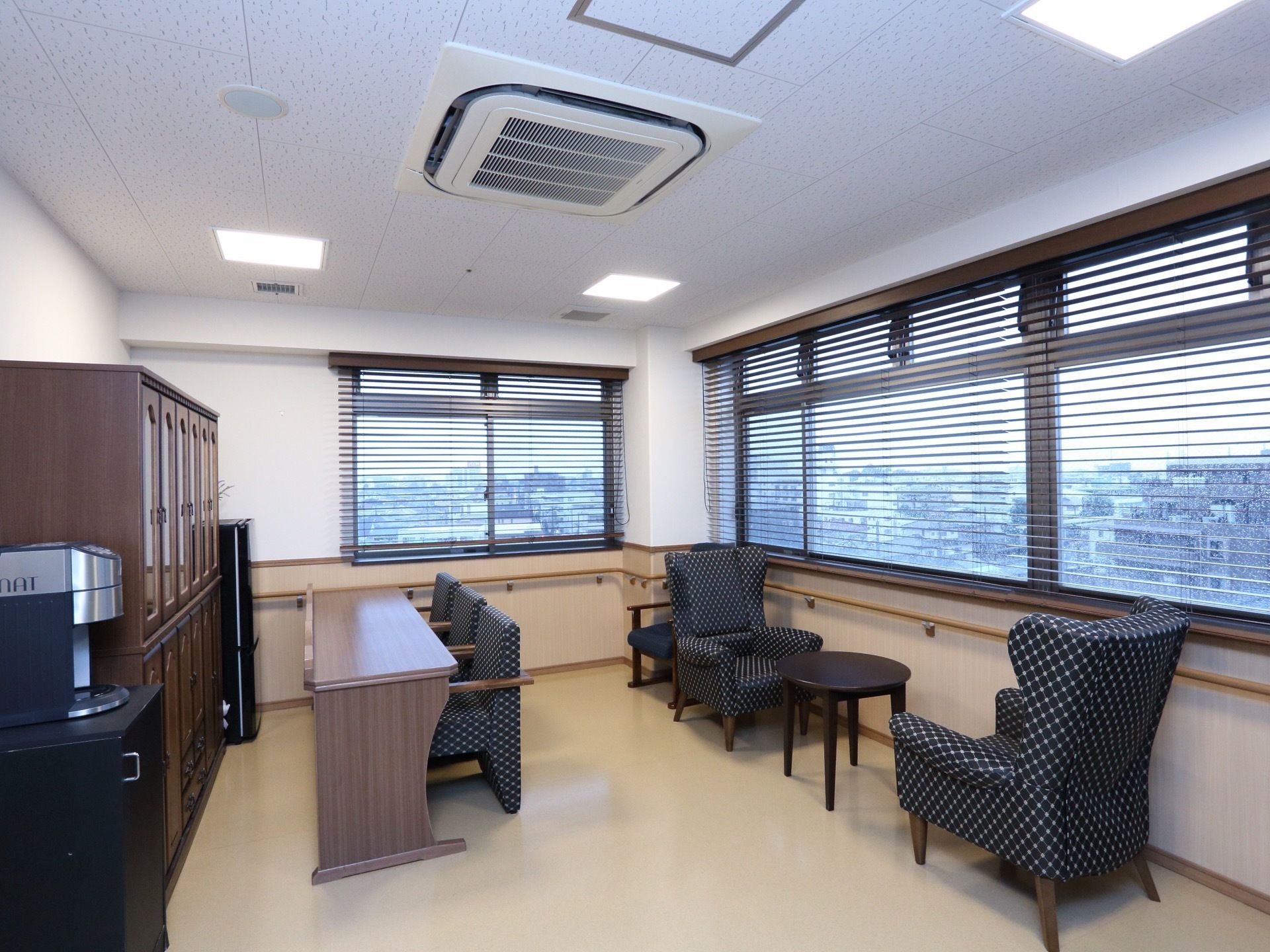 角部屋の２方向の壁のほとんどが腰高窓となっている。窓の下に手すりがある。一人掛けのソファセットが窓際にある。コーヒーメーカーと冷蔵庫がある。