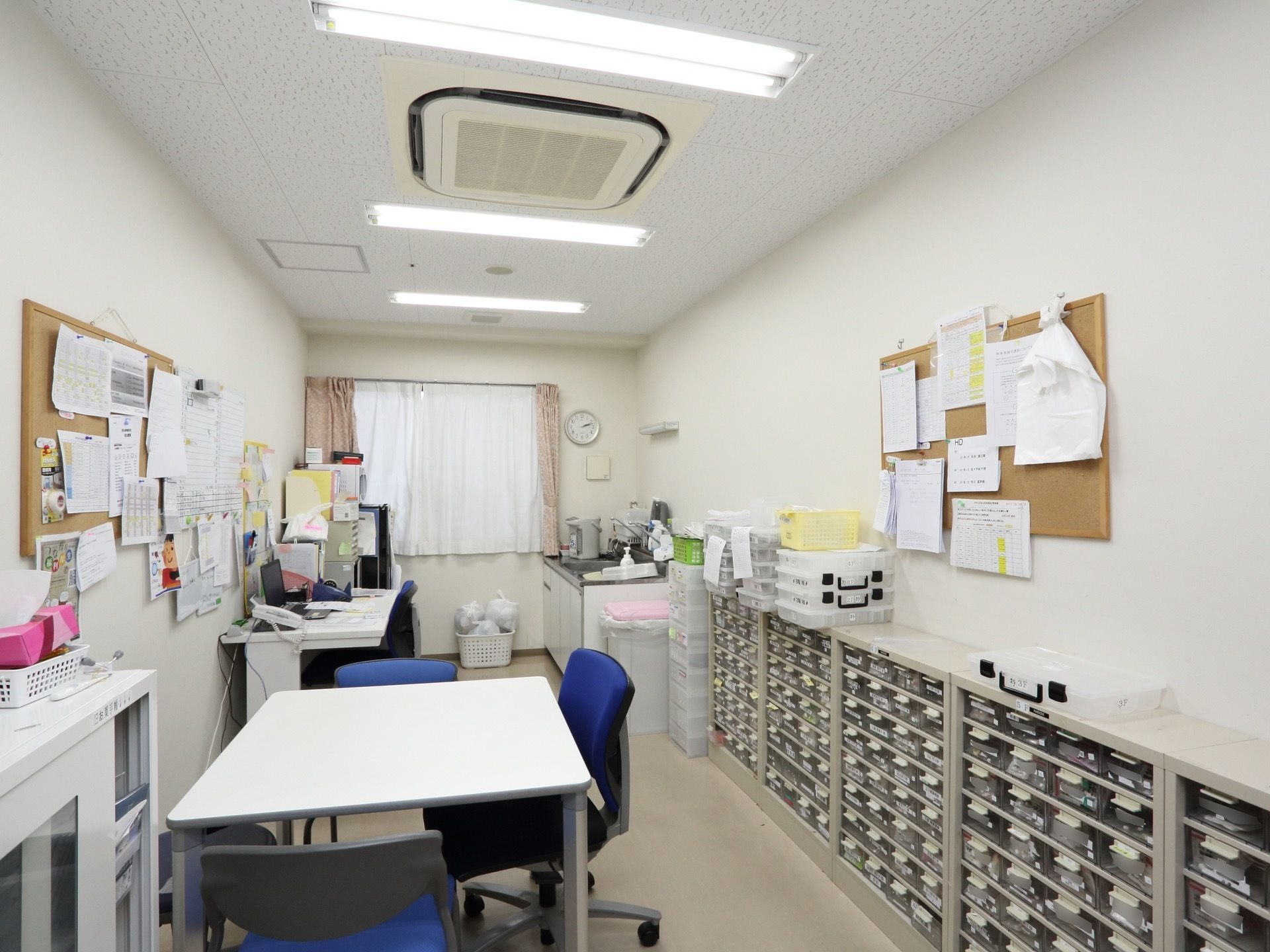明るいスタッフルームで、奥には給湯設備がありポットがおかれている。テーブルには電話やパソコンがあり、事務作業をすることができる。