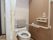 白で統一された清潔感のあるトイレである。便器には背もたれになるクッションが付いていて、手すりが完備されている。