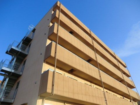 青空に向かってそびえたつ、非常階段が側面に見えている濃いベージュの建物