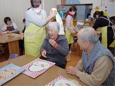 テーブルで福笑いをして楽しむ高齢者とエプロン姿のスタッフ