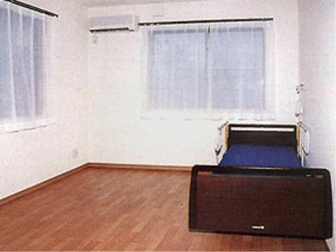 部屋の様子。壁は白色に統一され、左上にエアコンが設置されている。窓が２つあり、レースカーテンが引かれている。