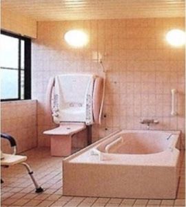 床や壁がピンク色のタイル貼りになっている浴室である。左側に大きめの入浴機器があり、シャワーが設置されている。