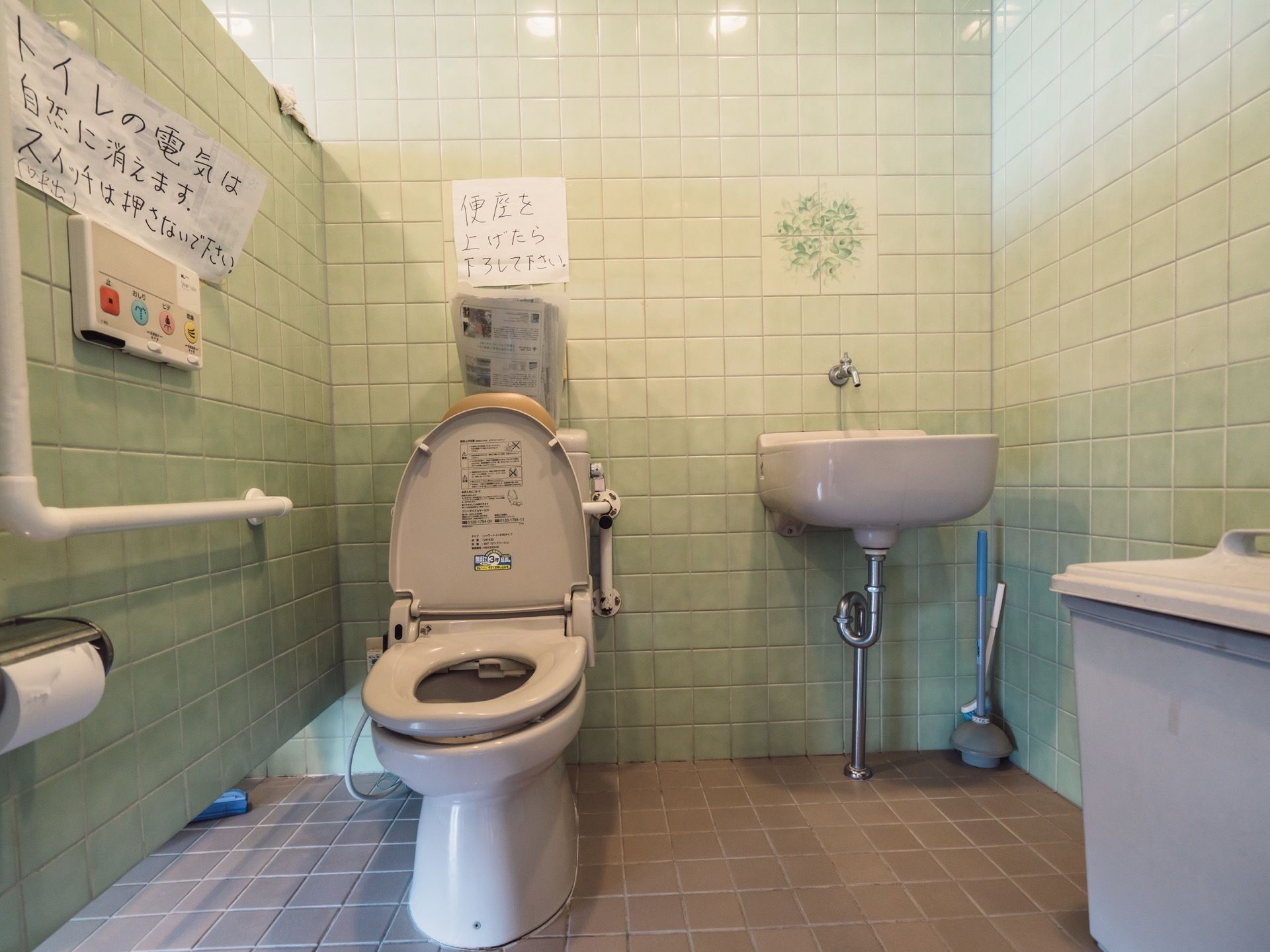 トイレのタンクや操作ボタンの上には張り紙があり、使用上の注意事項が書かれている。便座には温水洗浄機能が付いている。