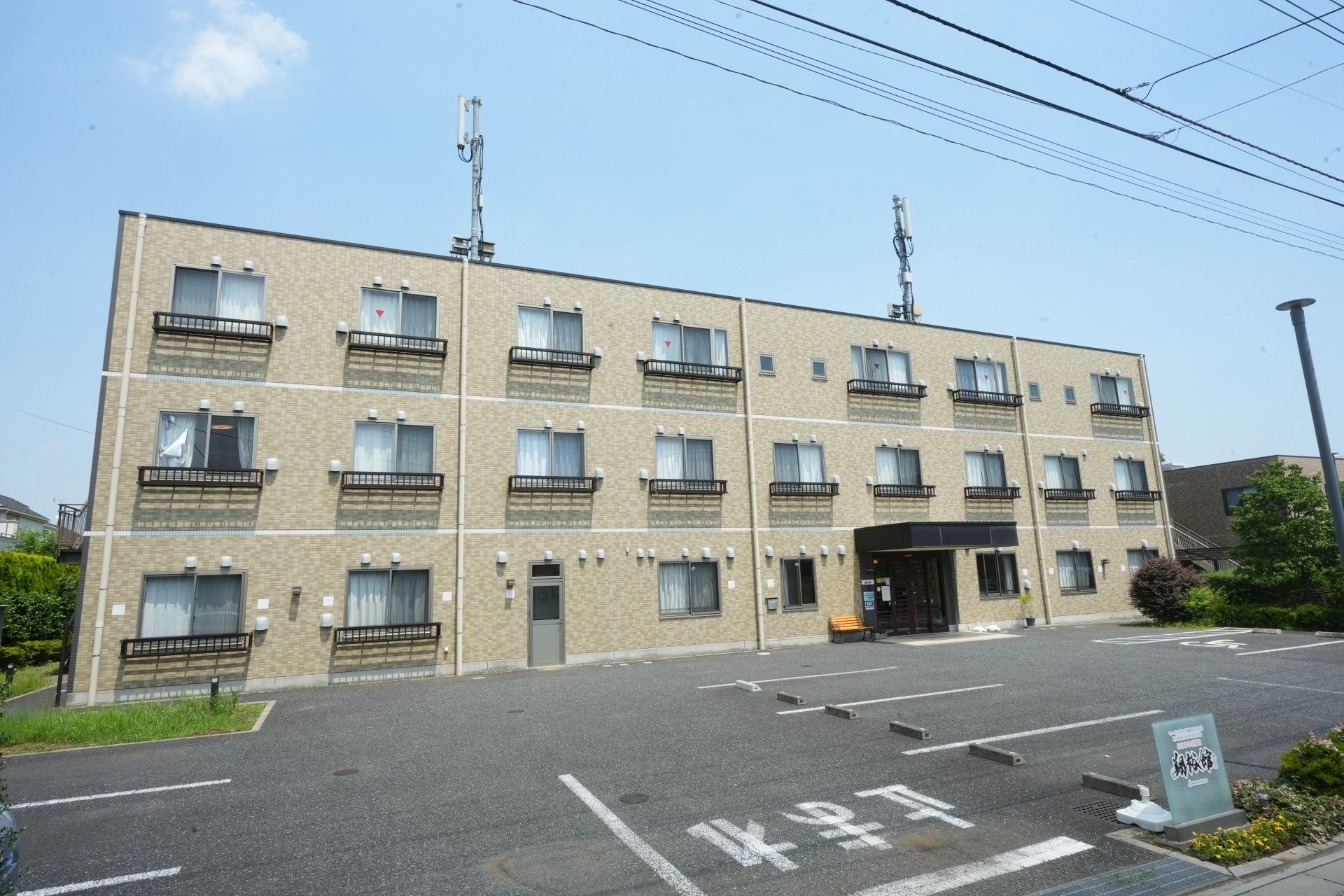 施設の建物のすぐ目の前に専用の駐車場が設けられている。車道との間に木の植え込みがある。街灯が設置されているので、夜間も安心である。