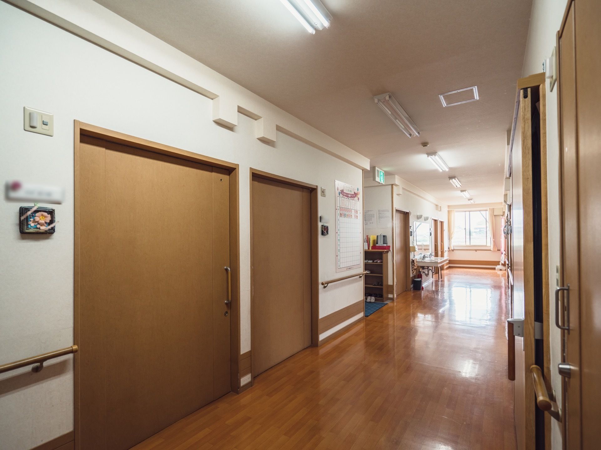 廊下は幅にゆとりがあり、車椅子をご利用の方も安心して通行できる。居室の扉も広々としている。清掃が行き届き、歩行の邪魔になるものもない。