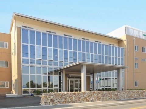 石の塀の奥に建つ、全面ガラス窓で近代的な雰囲気の3階建ての施設