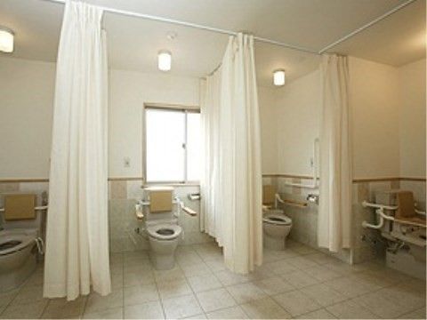 共用トイレは個室がカーテンで仕切られていて、緊急時もすぐにスタッフが対応できるようになっている。便器横には手すりもあり、安心して利用できる。