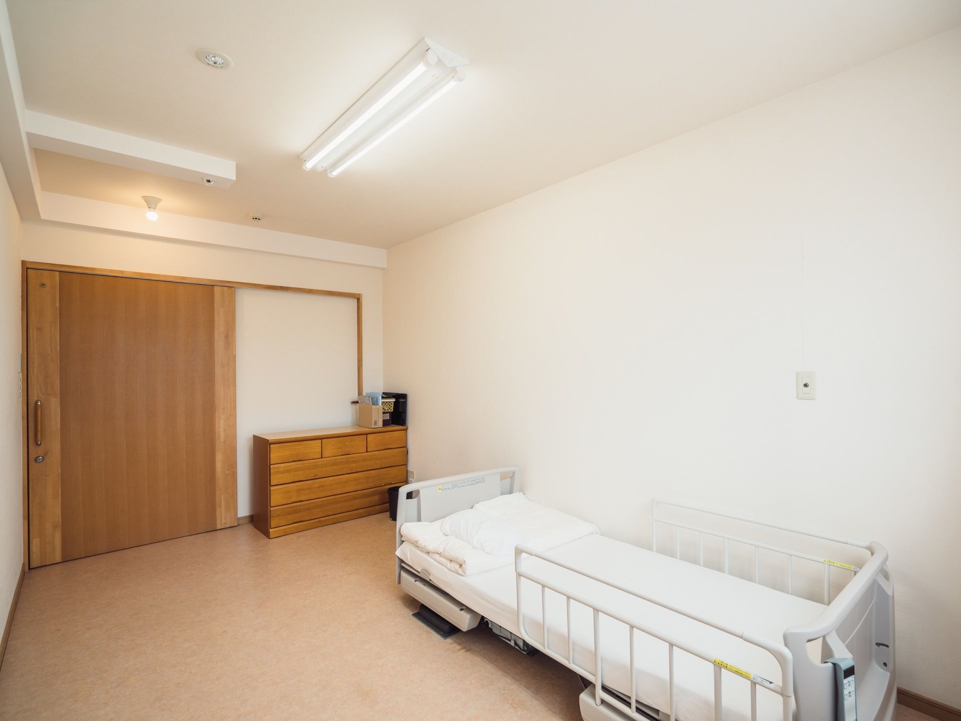 入居者様用の居室は、茶色と白色で統一された内装になっている。右側には木造のタンスとシングルベッドが用意されている。