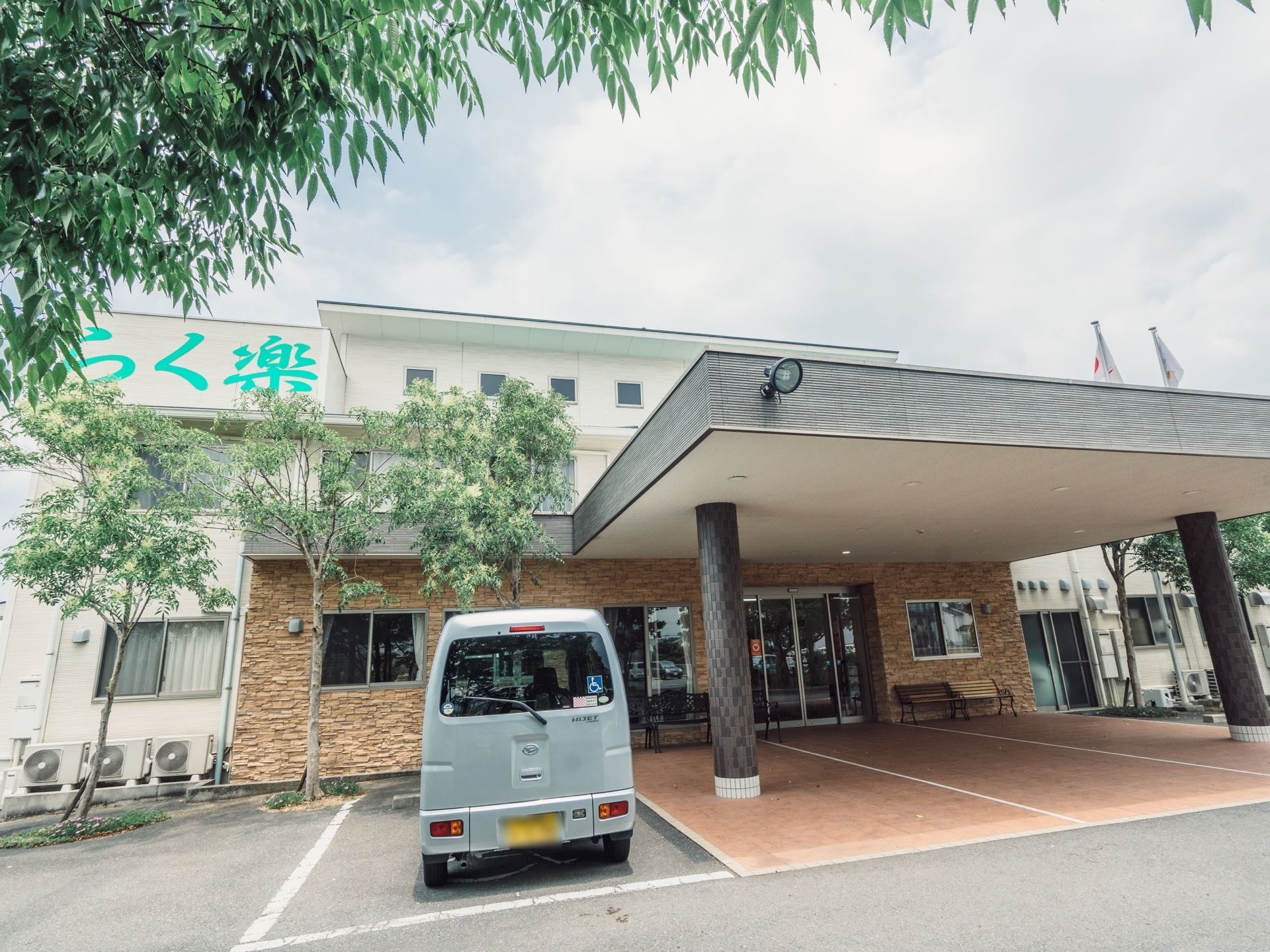 施設の入口はレンガ造りとなっており、大きな屋根が設置されている。玄関のそばには、シルバーの車が停められている。