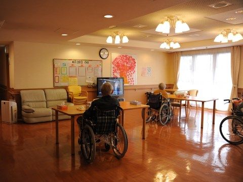 テーブルに向かいながら液晶テレビを鑑賞している人々が居るフローリングの広間