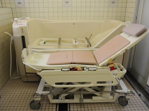 クリーム色のタイル張りの浴室の壁際に介護浴槽がある。寝たきりの方でも利用できる側面からセットするタイプのものである。