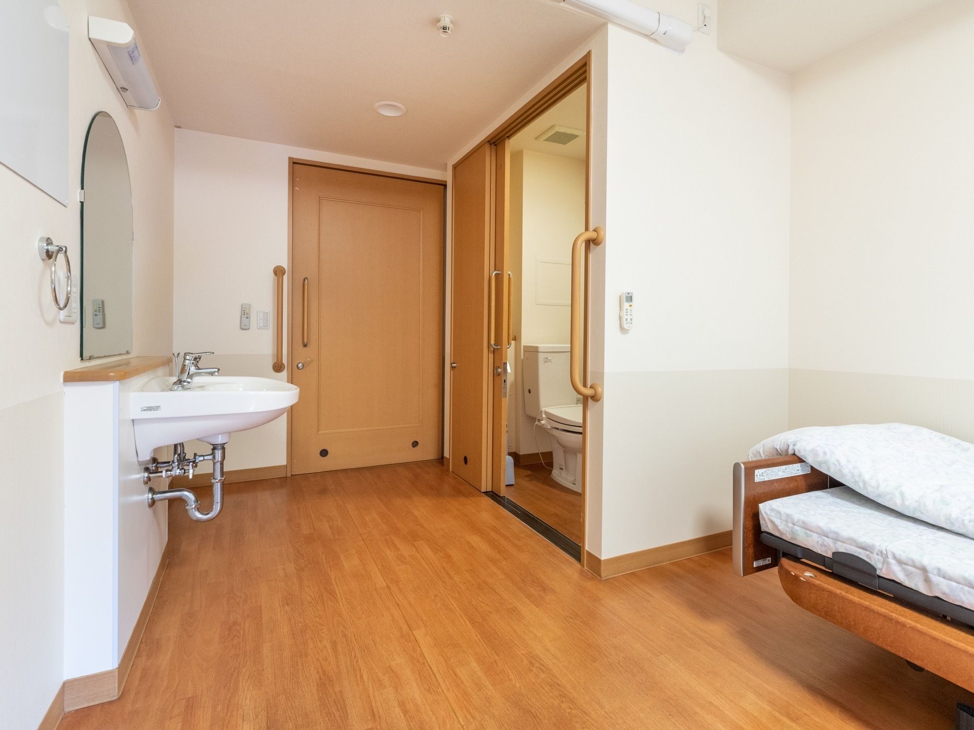 居室にはトイレと鏡を配した洗面台が備え付けられている。バリアフリーで清潔感あるフローリングのトイレである。