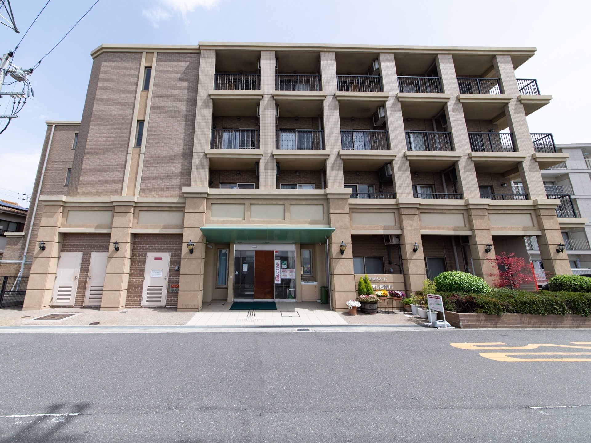 モカ色ベースの施設の外観。各居室に大きいベランダが付いているのが見られる。落ち着きのある住宅街なので、散歩に出かけることもできる。