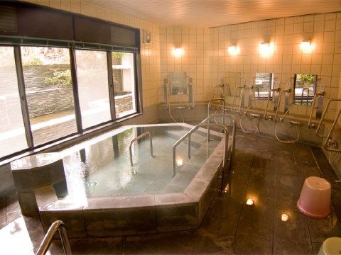 大きな窓があり複数のシャワーが設置されている石造りの大浴場