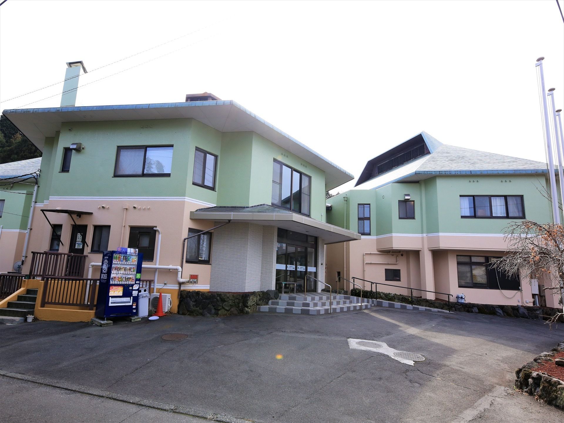 ２階建ての建物で、下がピンク、上がグリーンの外壁となっている。建物の左側には自動販売機が設置されている。