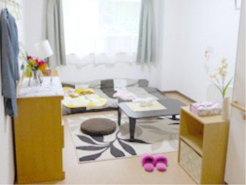 床に布団が敷かれている。テーブルの下にはカーペットがある。タンスの上に花瓶が置かれている。窓が大きく開放的な空間になっている。