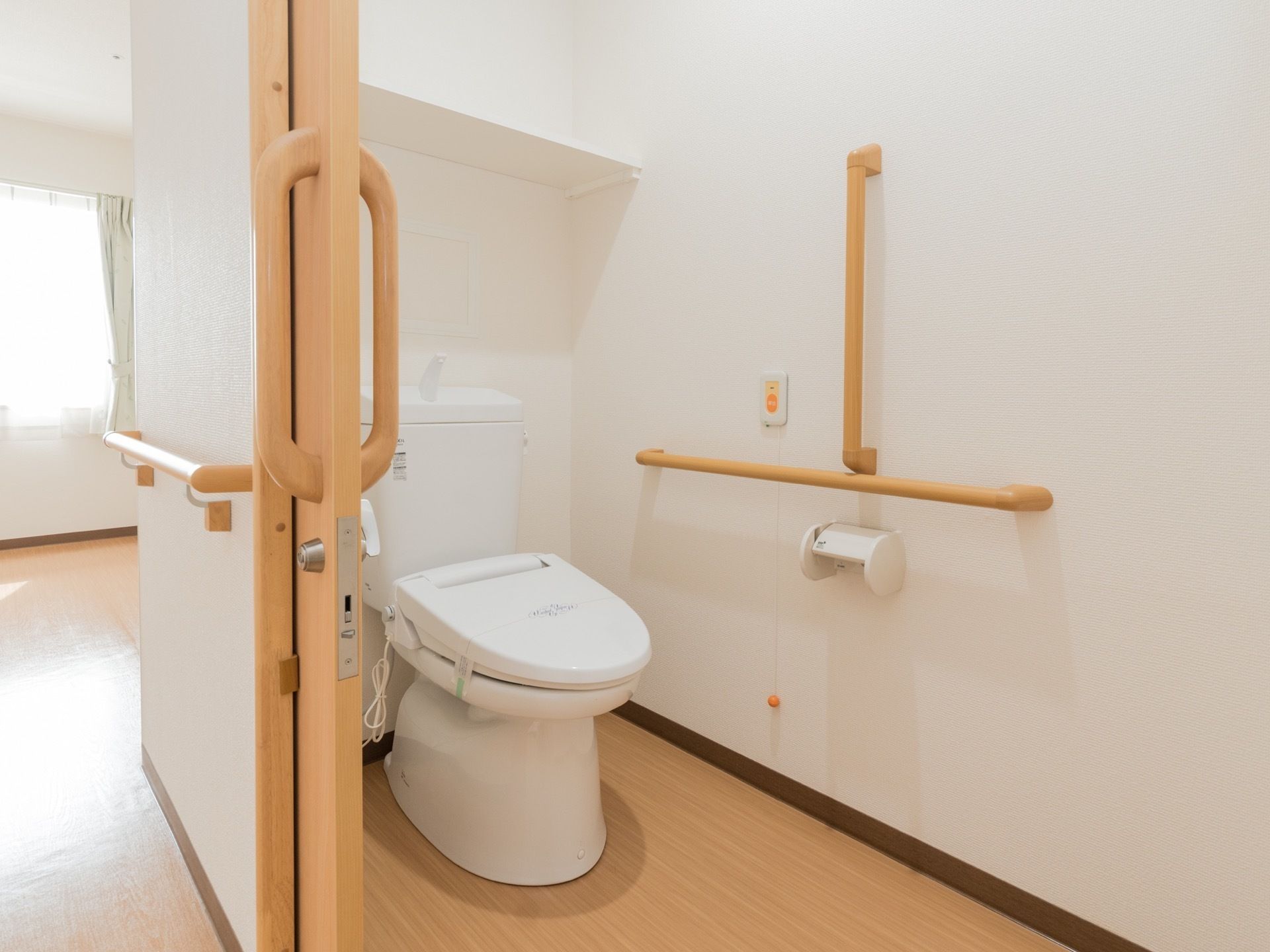 トイレには洋式便器が設置されている。縦型と横型の手すりが取り付けられた近くには呼び出しボタンが設置されている。