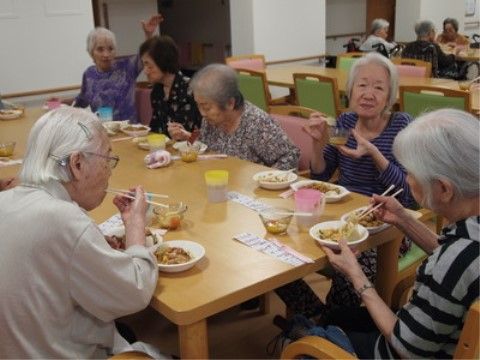 木製テーブルを囲むように座りながら食事や会話を楽しむ人々
