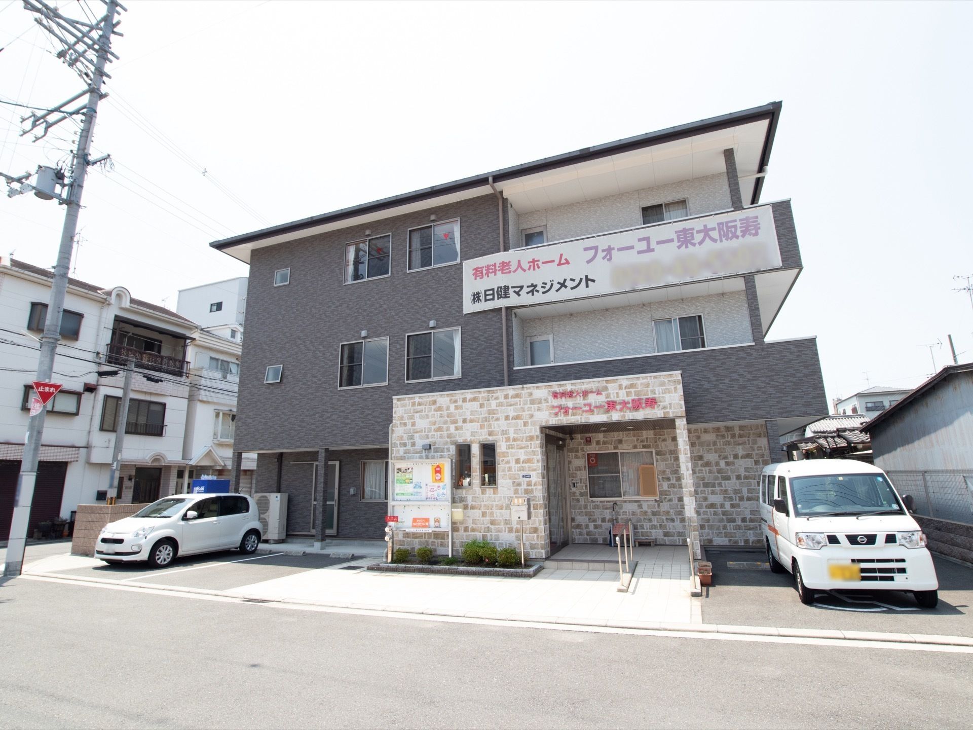 グレーの外壁に、レンガがモザイク柄に貼られた外観の建物である。３階部分に大きく看板が貼りだされている。