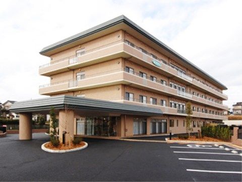 アスファルトで舗装された駐車場に囲まれた４階建ての建物