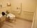 広いスペースにトイレがある。入口から便器まで、壁に手すりが設置されている。トイレットペーパーの予備が棚板の上のかごに積まれている。