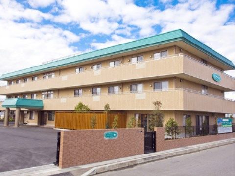 道路沿いの舗装された敷地に建っている３階建ての施設
