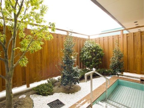 植栽が施され白い砂利が敷き詰められた庭園と、手すりが設置された露天風呂