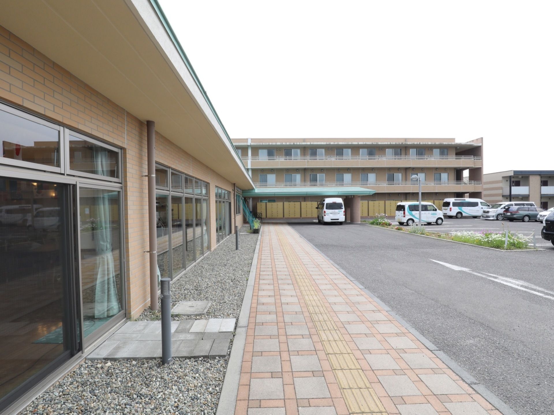 施設に隣接している平面駐車スペース。建物入口側の通路が広くなっている。歩行者用通路には点字ブロックが設置されている。