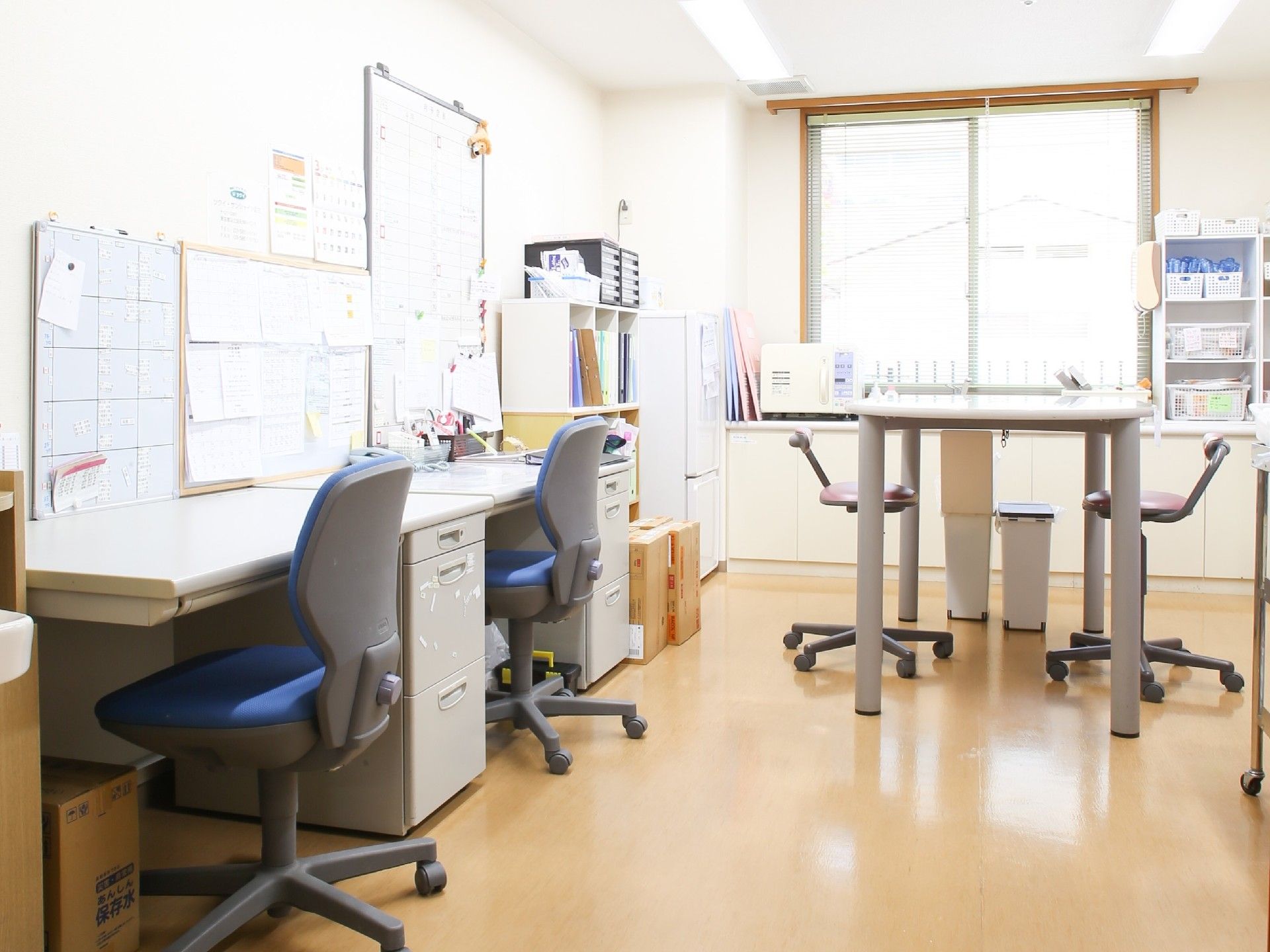 職員用の室内には、いくつも机や椅子がある。また、壁にはホワイトボードやプリントが貼ってあるボードが設置されている。