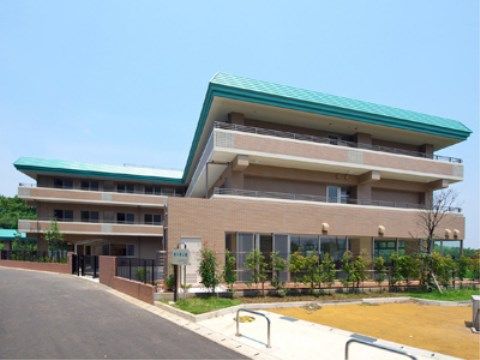 植栽スペースとアスファルトで舗装された敷地に囲まれた３階建ての建物