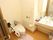 ピンクのトイレットマットが敷いてあるトイレで、洗浄済みの紙が便座には取り付けてある。手すりが両脇に設置されている。