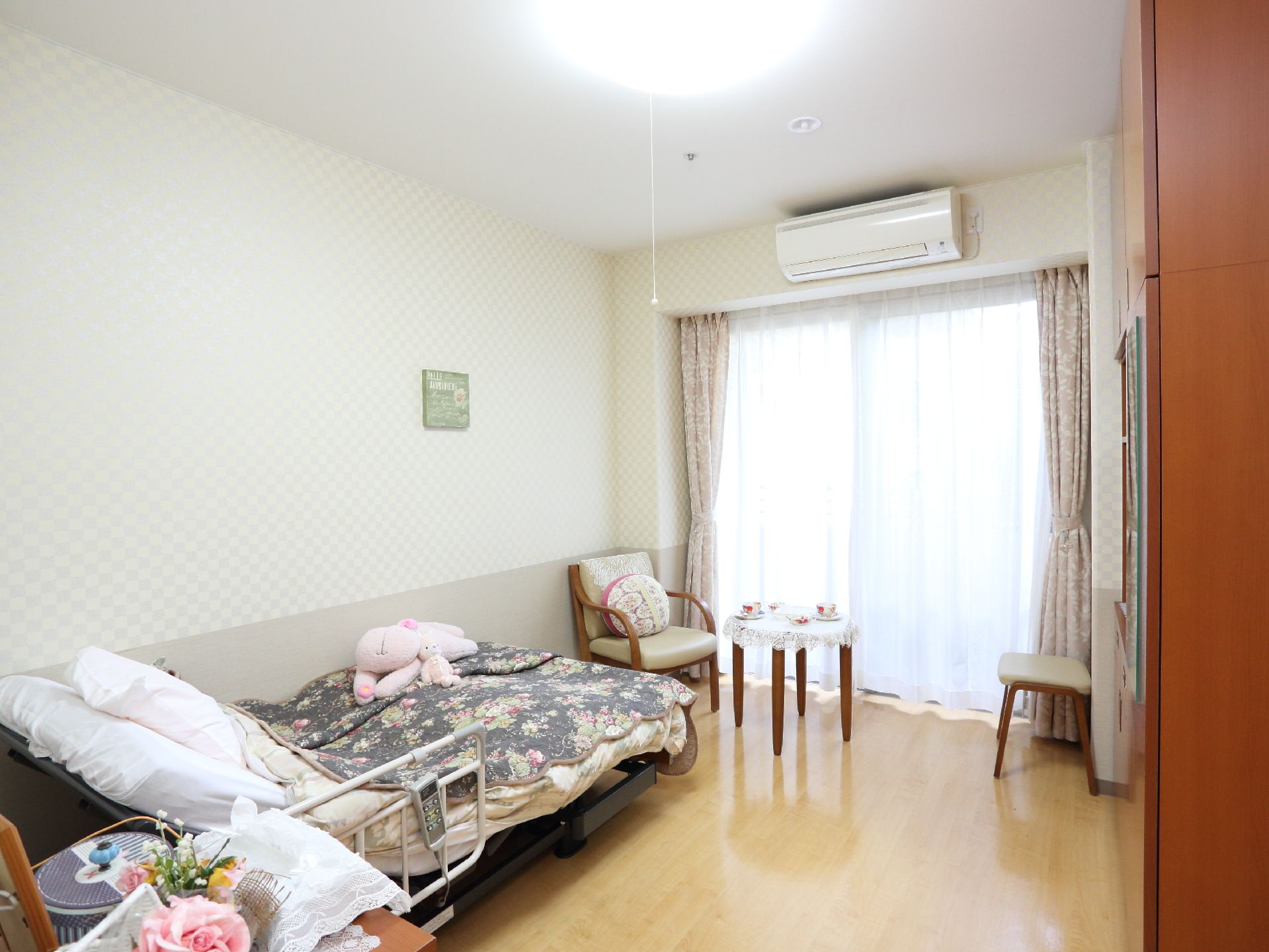 居室に置いてあるベッドは電動式になっているので、立ち居が楽である。クロスのかかったラウンドテーブルに肘掛椅子が窓際にある。