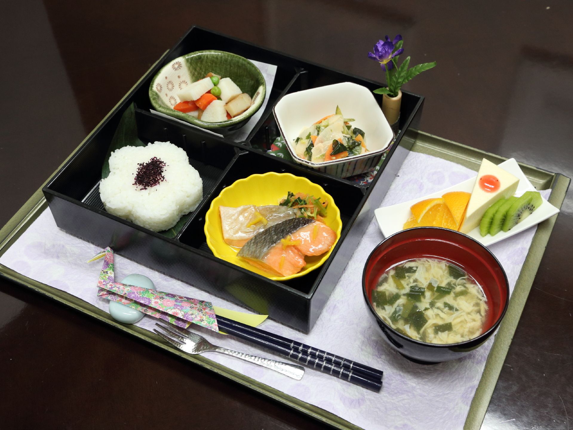 会席風の食事が盆に乗っている。竹の花瓶に花が挿してある。小鉢などの配色なども考えた食事となっている。