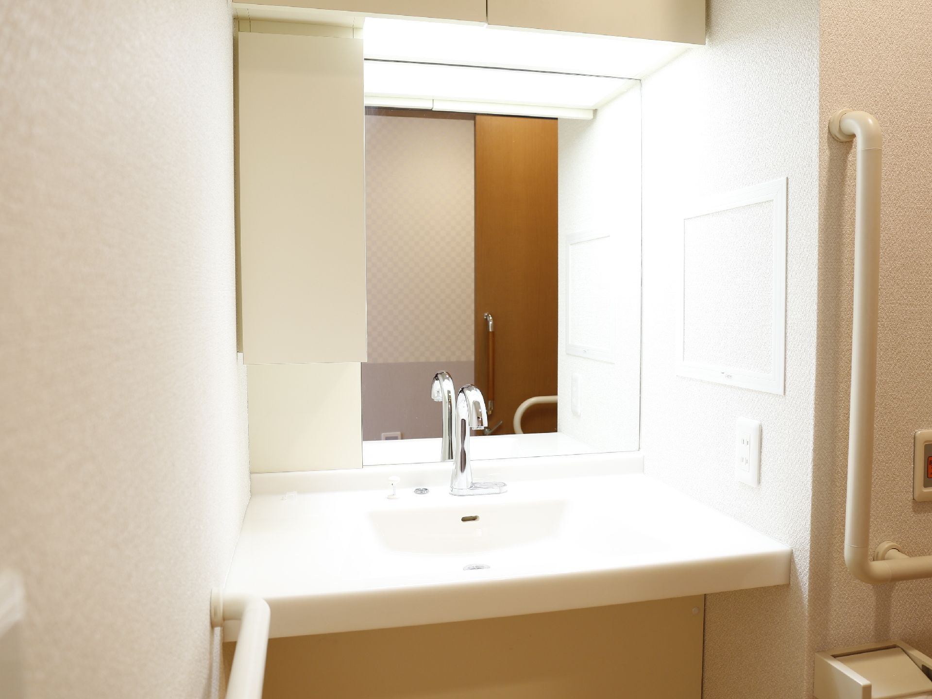 大面鏡がついた洗面台には手すりがついている。トイレットペーパーホルダーがついている壁上に、職員を緊急時に呼ぶことができるブザーがある。