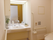 白色の壁と明るい木目の床のトイレである。壁には手すりが設置してある。横側には、洗面台が備えられている。