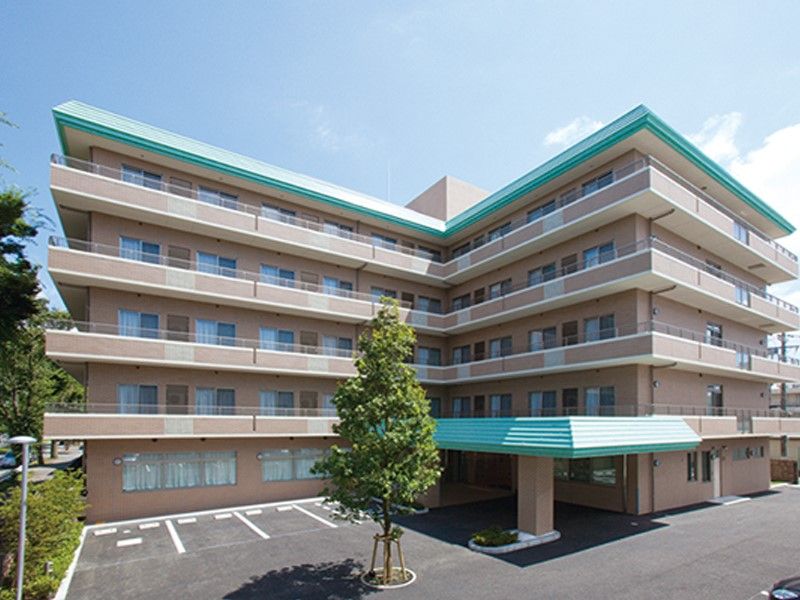ベージュが基調になった、Ｌ字型の５階建ての建物。入口前と最上階のひさしの部分だけが薄緑色になっている。