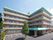 ベージュが基調になった、Ｌ字型の５階建ての建物。入口前と最上階のひさしの部分だけが薄緑色になっている。