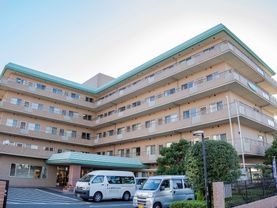薄いブラウンの外壁にグリーンの屋根の５階建ての外観である。敷地内には、駐車スペースを設け、豊富な植栽を取り入れている。