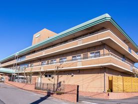 建物の前には車が通ることができるスペースがあり、道路側には壁と柵が取りつけられている。壁の前には、樹木が植えられている。